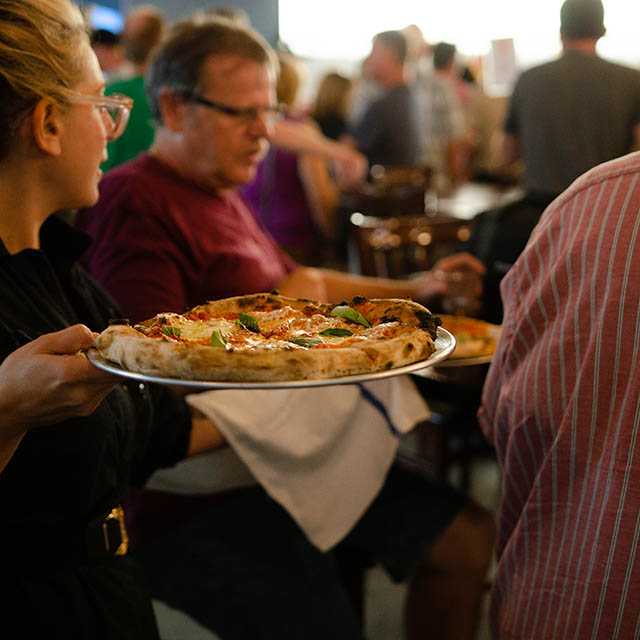 a server bringing pizza to a table in the tasting room